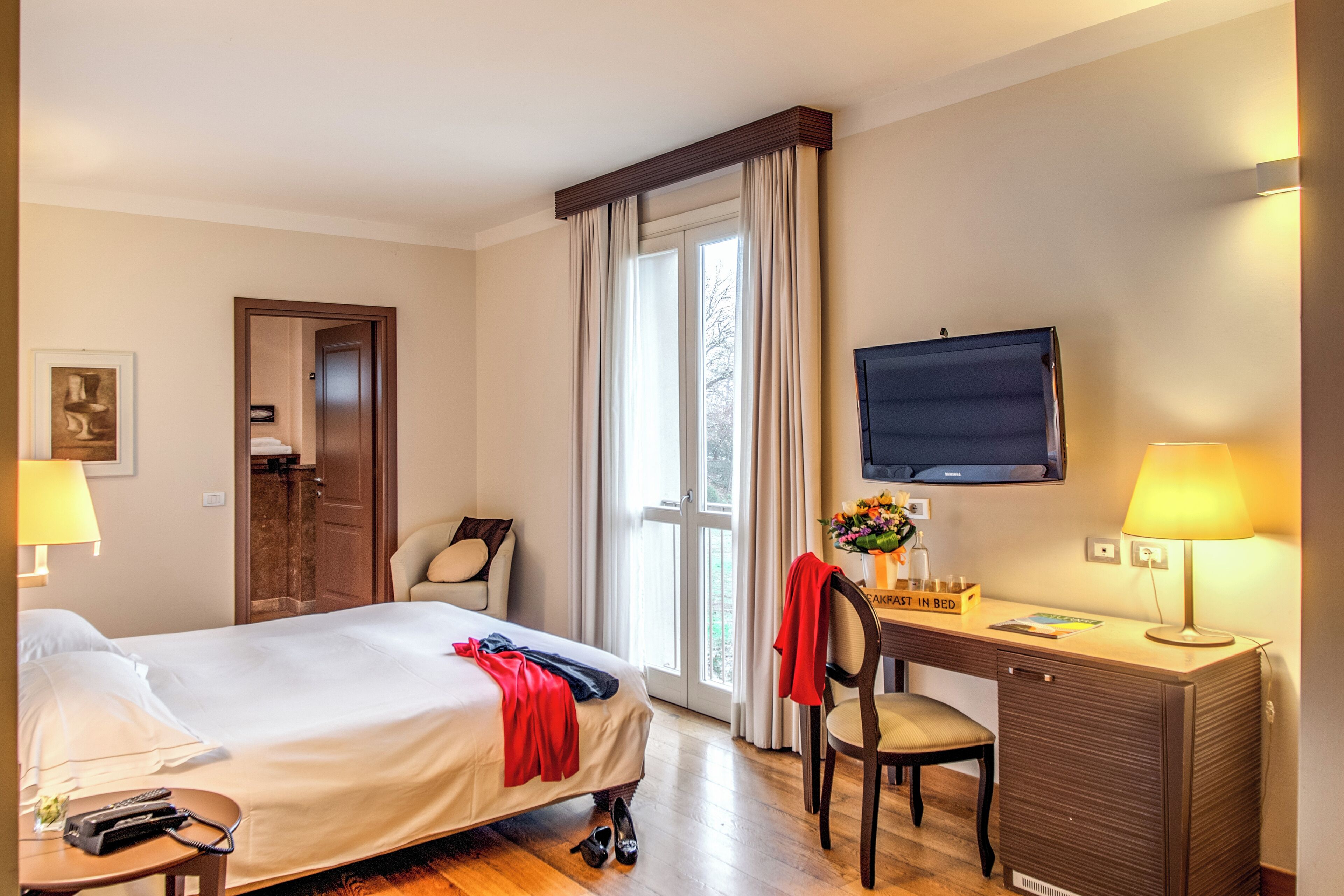 Een hotelkamer met een bed, bureau, stoel, televisie en een raam met gordijnen.