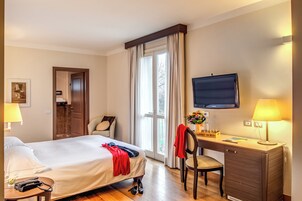A hotel room with a bed, desk, chair, TV, and a window with curtains.