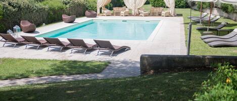 A rectangular swimming pool with lounge chairs and a covered seating area.