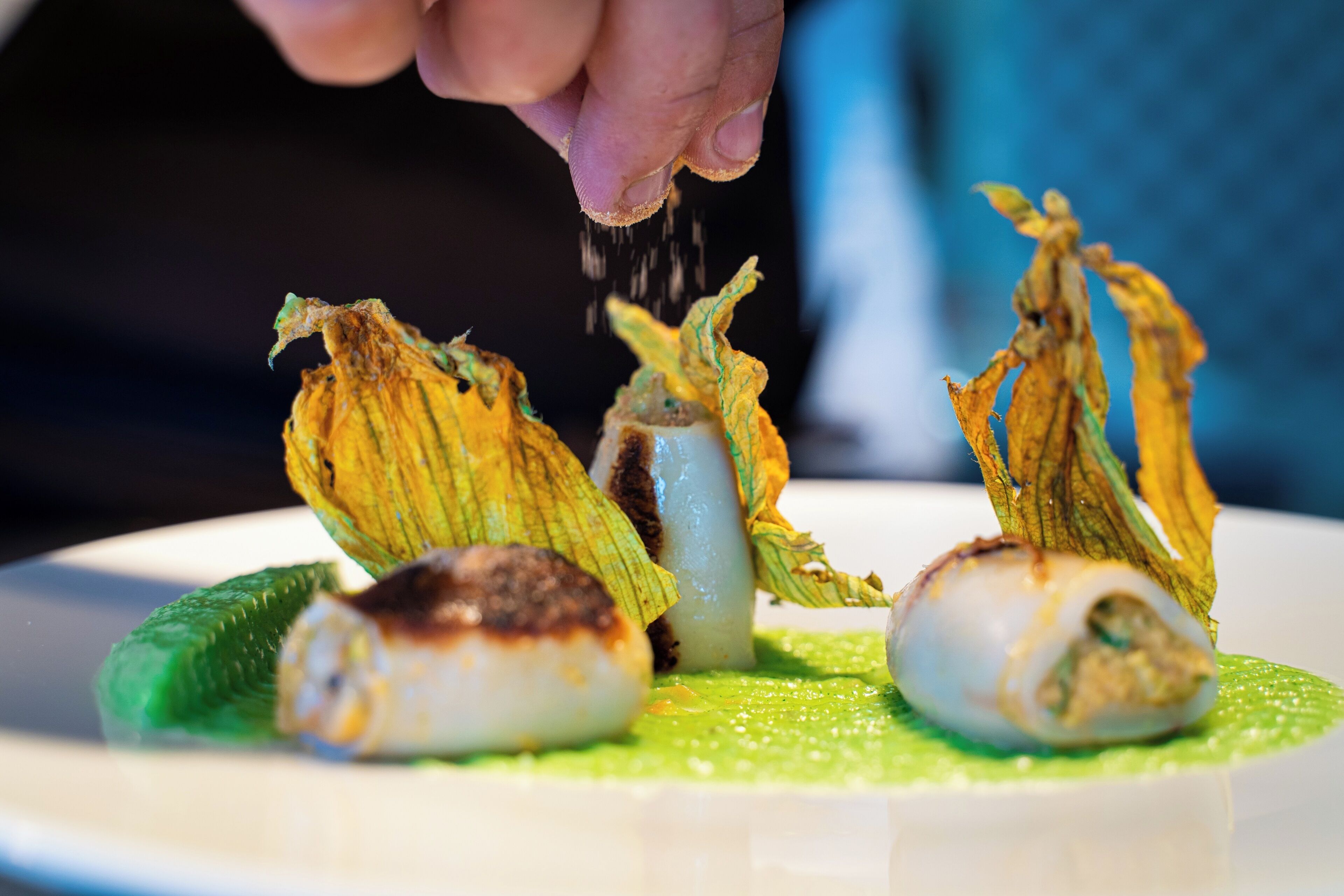 Une assiette contenant divers aliments, notamment une noix de Saint-Jacques, un morceau de viande et un légume, le tout agrémenté d’une sauce verte.