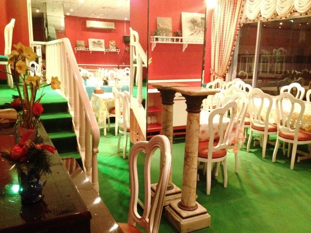 Un restaurant avec des chaises blanches et une moquette verte. On y trouve des tables et un vase rempli de fleurs, placés à gauche.