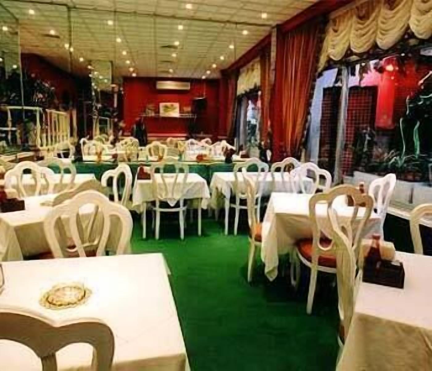 A restaurant with white chairs and tables, green carpet, and red walls.
