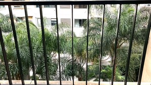 Un balcó amb una cadira de plàstic blanc, amb vista a un edifici residencial amb diverses finestres i aparells d'aire condicionat.