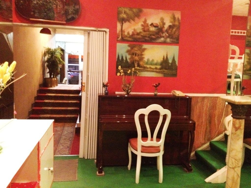 A room with a piano, a white chair, a desk, and a staircase leading to another room.