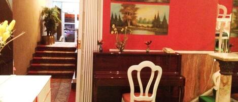 A room with a piano, a white chair, a desk, and a staircase leading to another room.