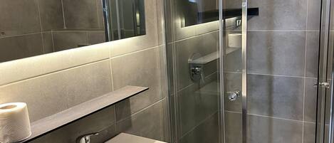 Uma casa de banho moderna com chuveiro em cabine de vidro, lavatório branco e espelho sobre o lavatório.