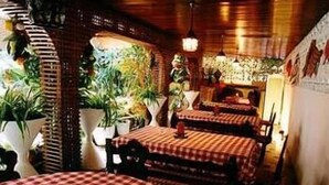 Interior de restaurant amb taules rodones cobertes amb mantells a quadres vermells i blancs, cadires de fusta i plantes en testos.