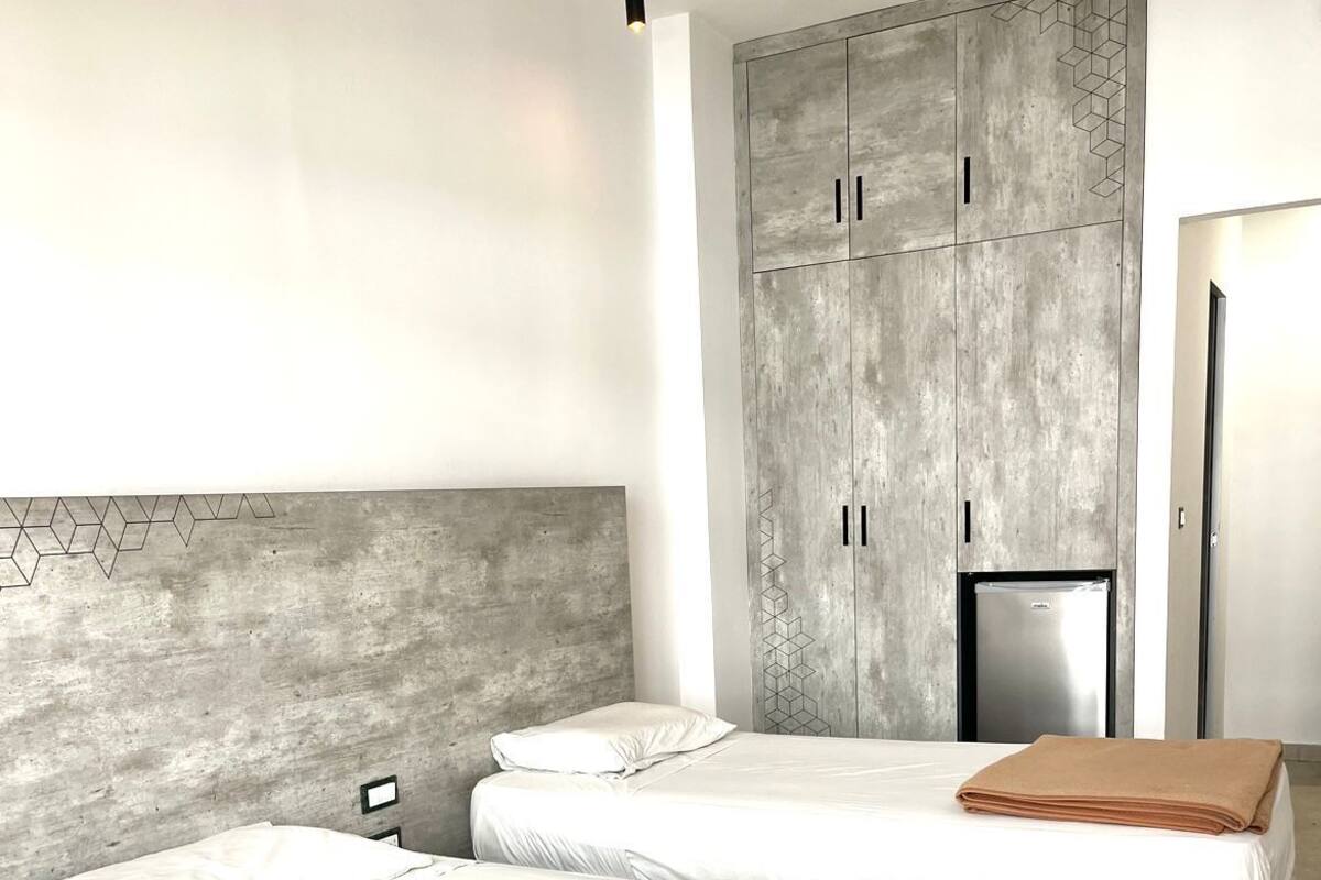 Et moderne hotelværelse med to senge, et klædeskab og et køleskab.
