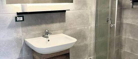 A modern bathroom with a glass shower enclosure, a white sink with a wooden cabinet, and a mirror above the sink.