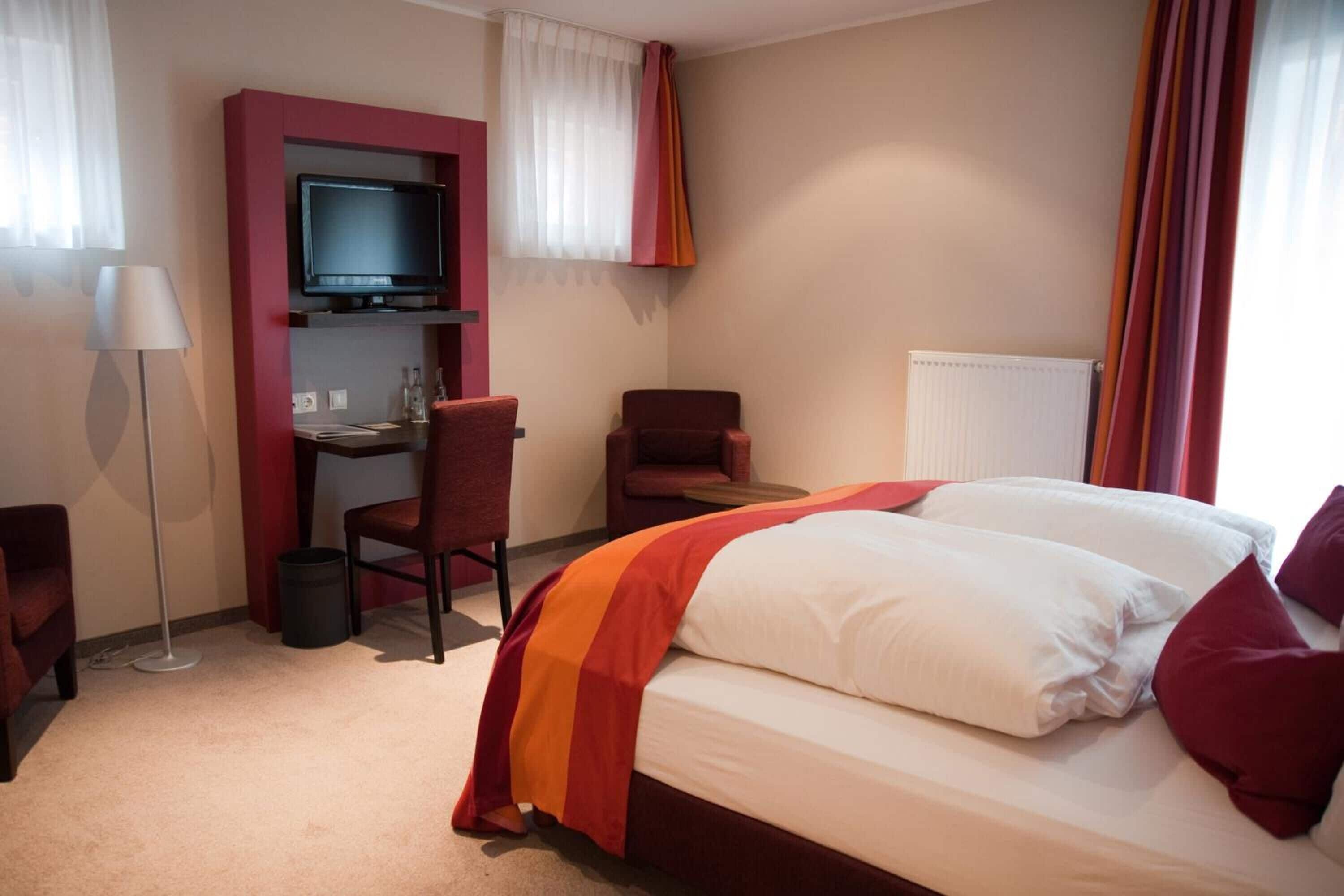 Ein Hotelzimmer mit Bett, Schreibtisch, Stuhl, Fernseher und Heizkörper.