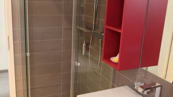 A bathroom with a glass-enclosed shower, a white sink, and a red medicine cabinet.