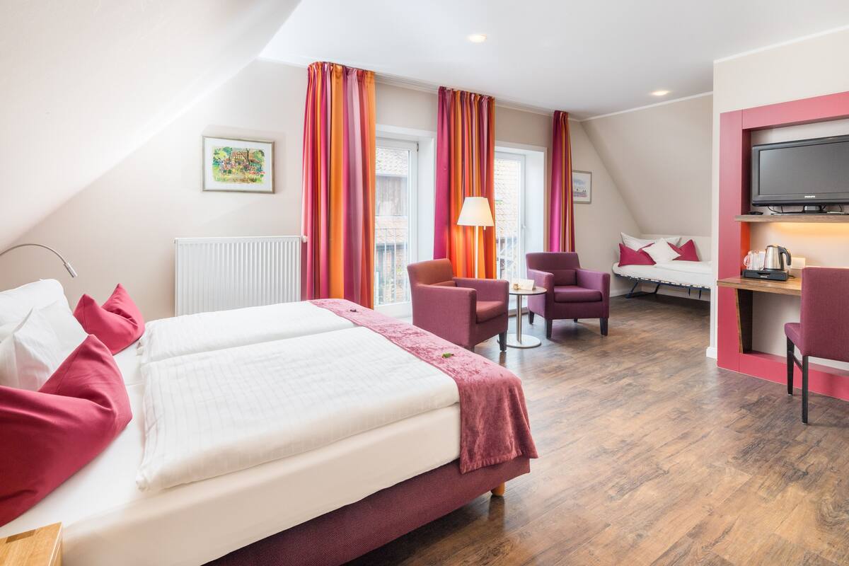 Een hotelkamer met een bed, een bureau met een televisie, een stoel, een klein tafeltje en een raam met gordijnen.