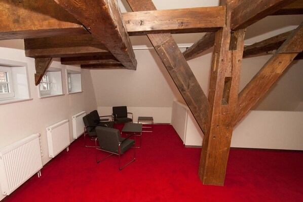A room with a red carpet, wooden beams, white radiators, and black chairs. - Hotel Am Kloster (Wienhausen)
