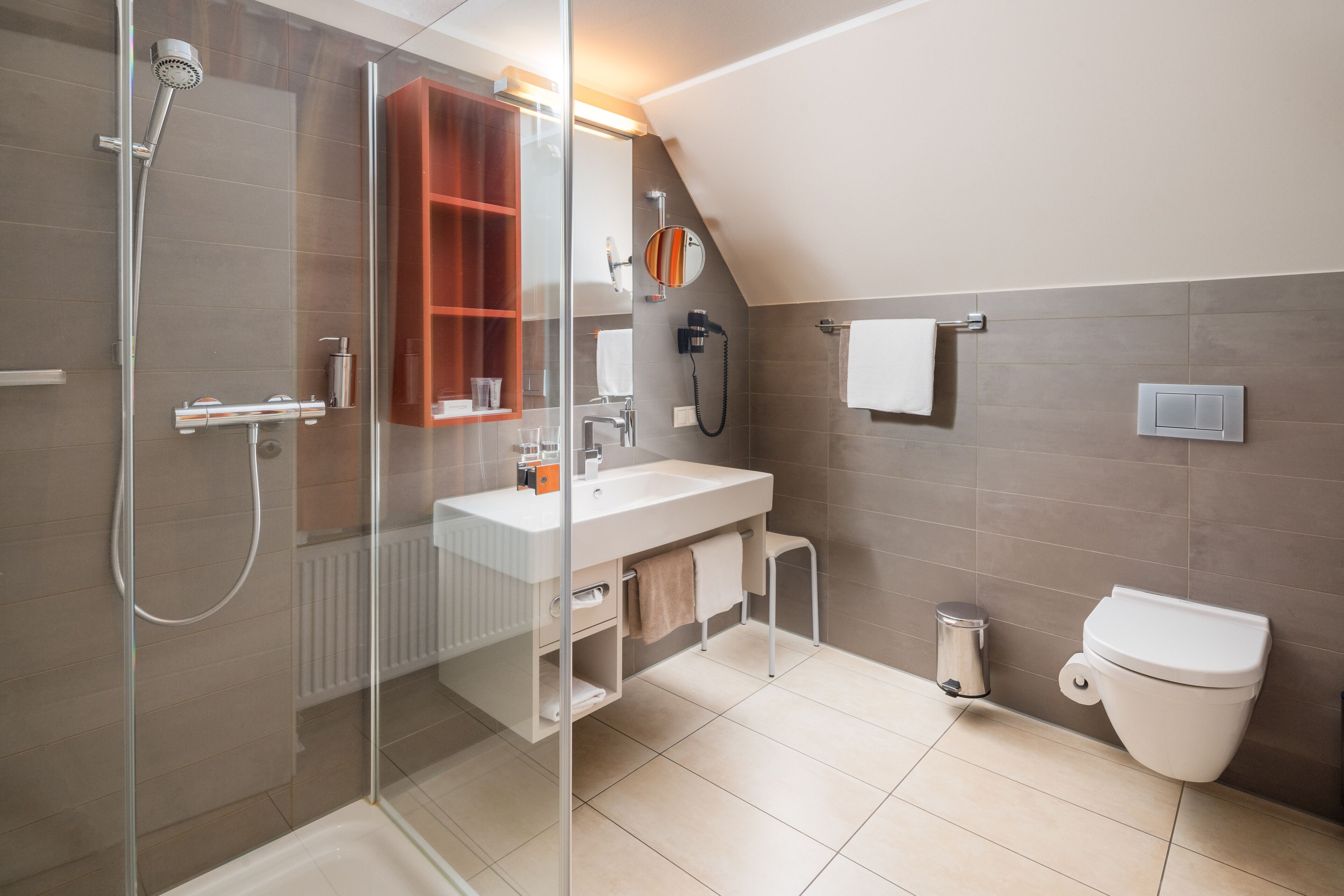 Un baño moderno con cabina de ducha de vidrio, un lavamanos blanco, un inodoro y un armario de madera.
