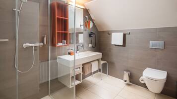 Un baño moderno con cabina de ducha de vidrio, un lavamanos blanco, un inodoro y un armario de madera.
