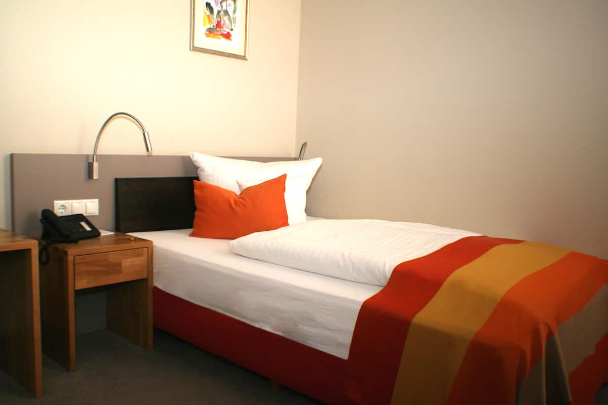 Een hotelkamer met een bed, een bureau, een telefoon en een schilderij aan de muur.