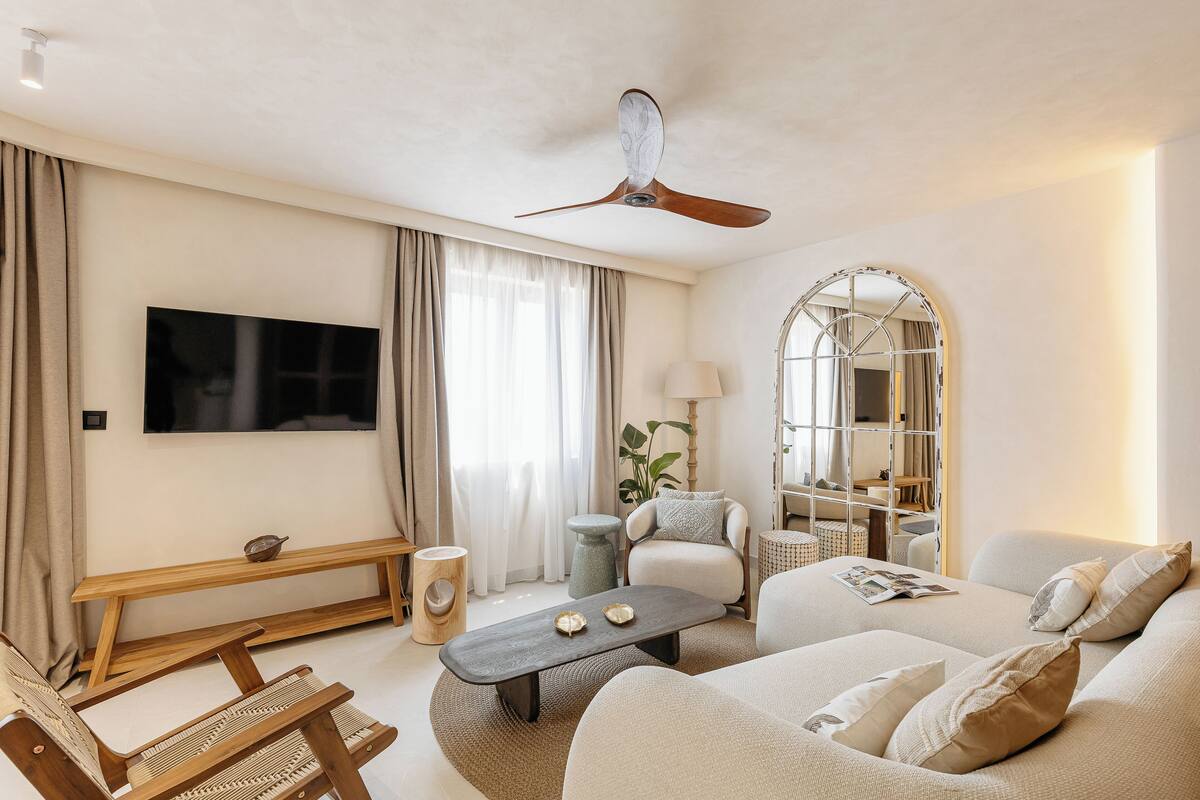A living room with a flat-screen TV, a ceiling fan, a sofa, a coffee table, and a bench.
