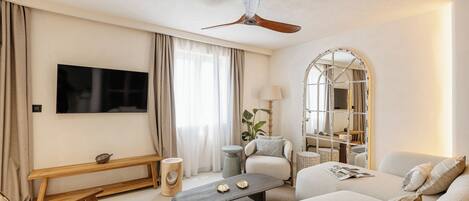 A living room with a flat-screen TV, a ceiling fan, a sofa, a coffee table, and a bench.