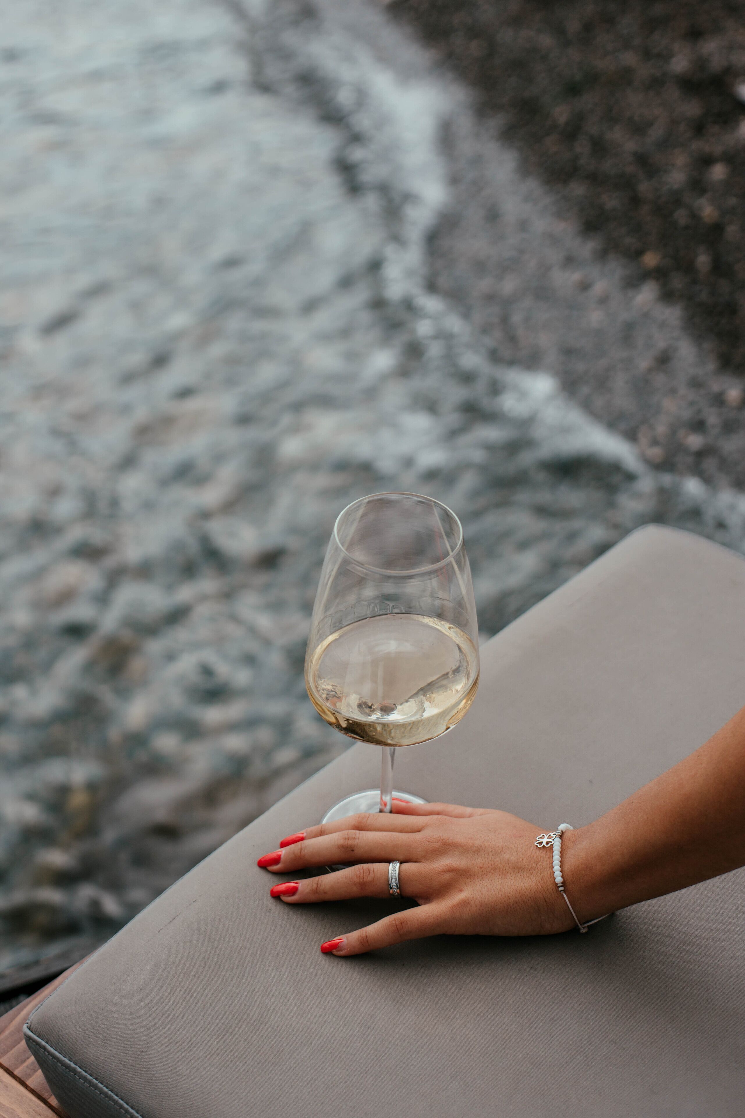 Une main posée sur un pouf gris, à côté d’un verre de vin blanc.