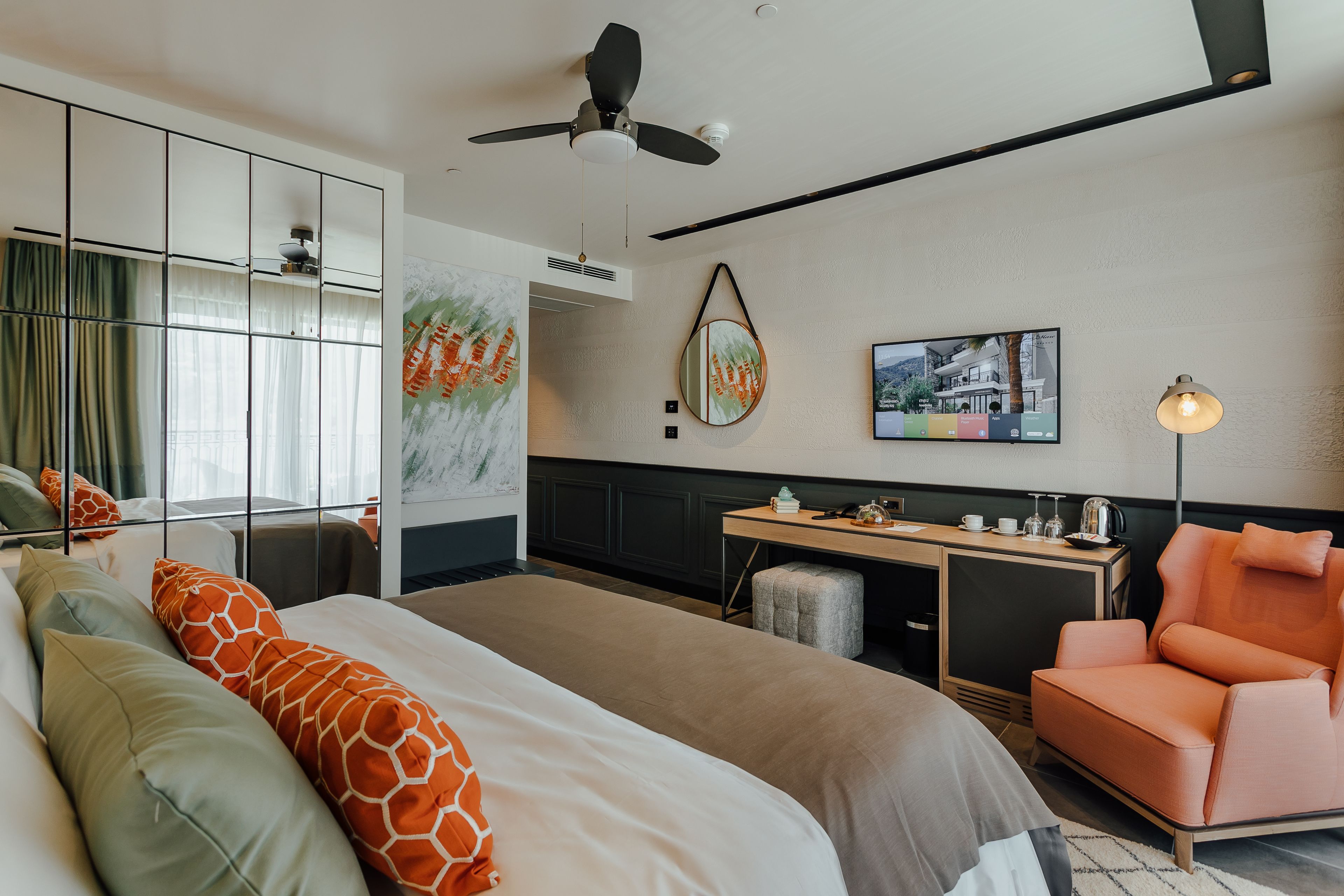 Una habitación de hotel con una cama, un escritorio, una silla, un ventilador de techo y obras de arte en las paredes.