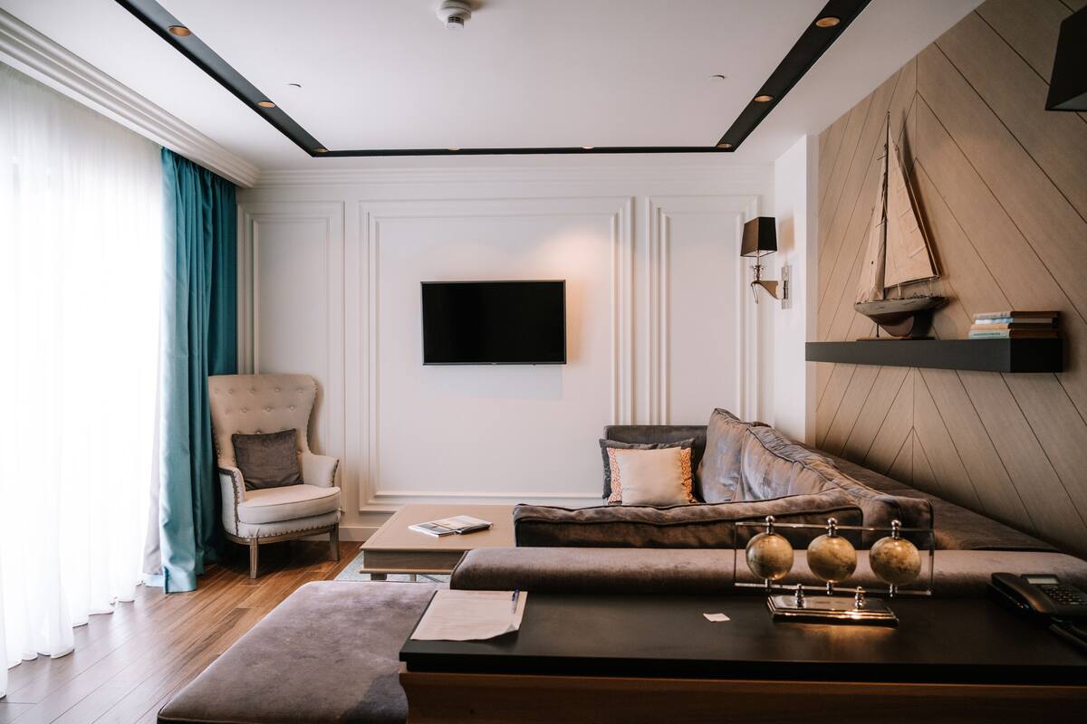 A modern living room with a sofa, armchair, and coffee table. A flat-screen TV is mounted on the wall, and there is a decorative sailboat on a shelf.