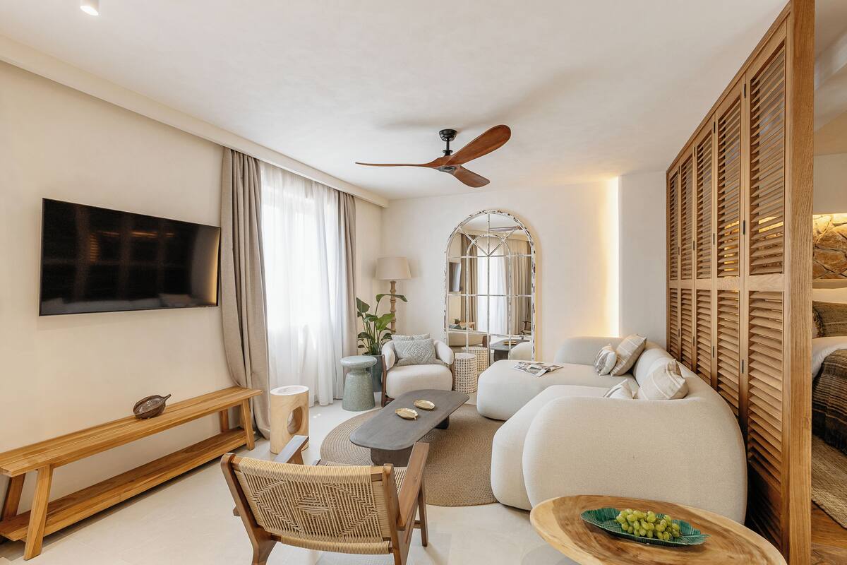 A modern living room with a flat-screen TV, wooden furniture, a ceiling fan, and a large mirror.