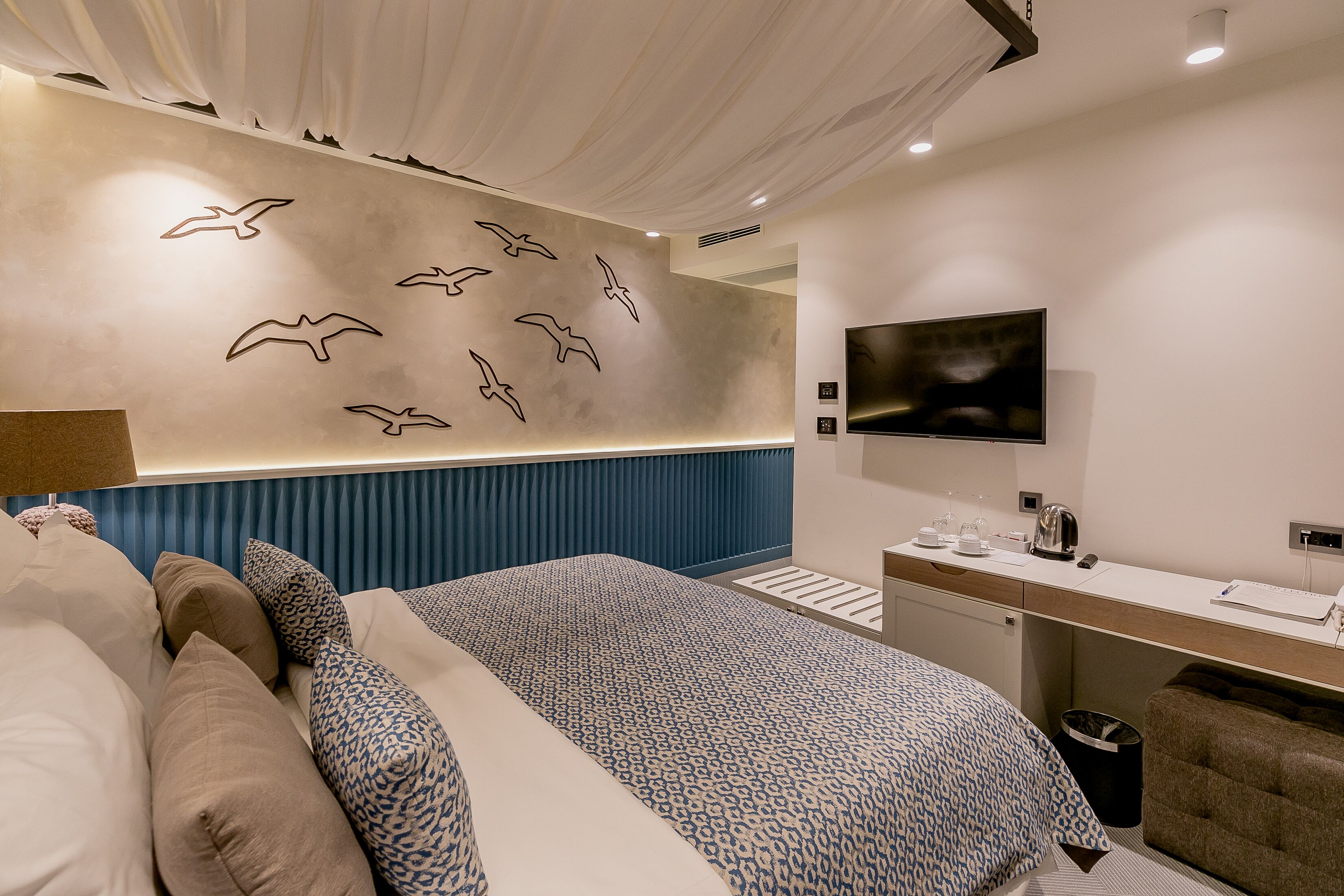 Une chambre d’hôtel moderne dotée d’un grand lit, d’un bureau avec un téléviseur à écran plat et d’un mur orné de silhouettes d’oiseaux.