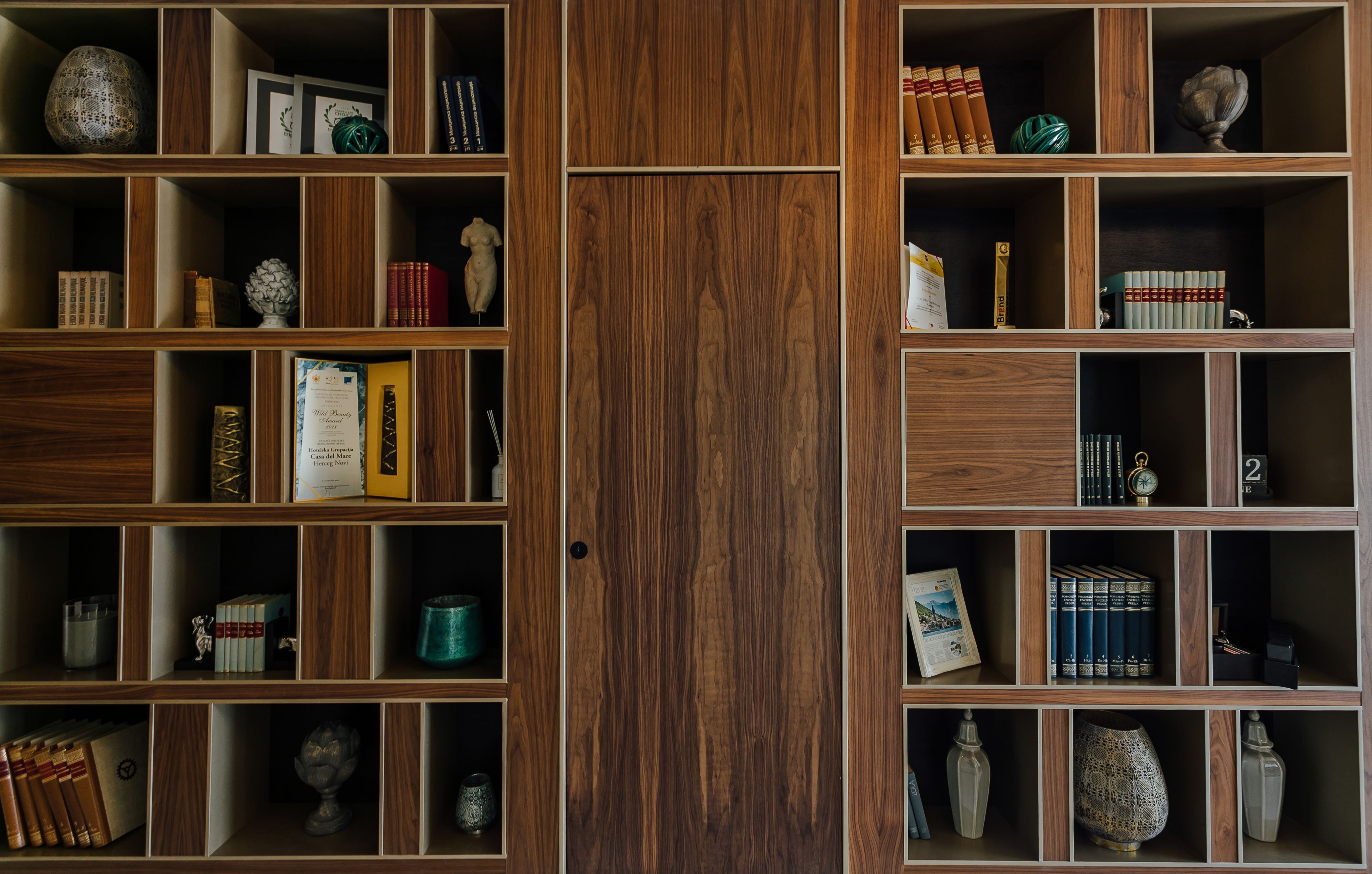 Una estantería de madera con varios compartimentos, cada uno con libros, adornos y pequeñas esculturas.