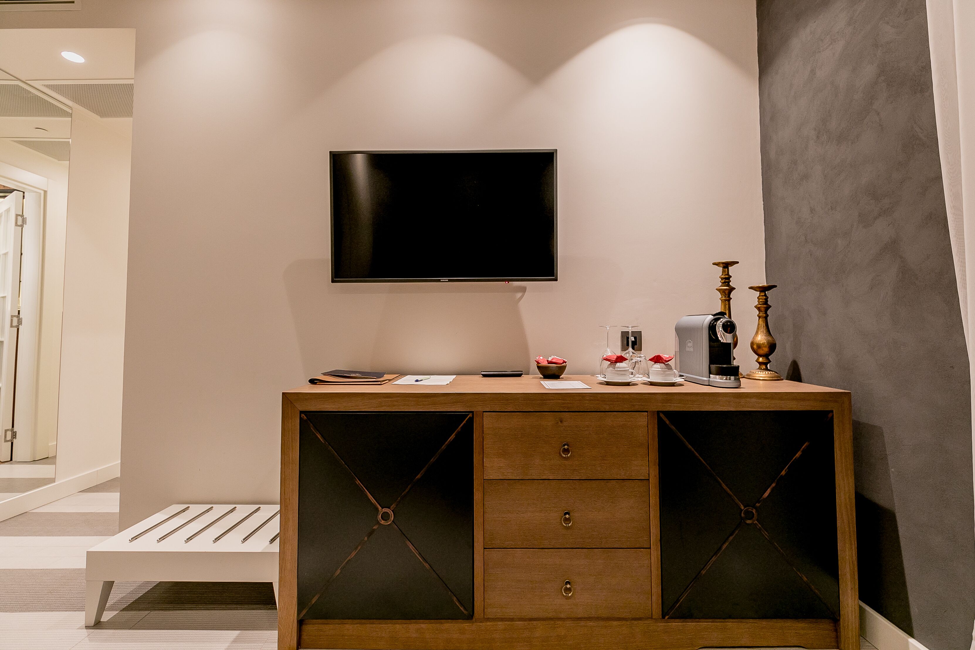 A modern room with a wooden cabinet, a flat-screen TV mounted on the wall, and a small table with decorative items.