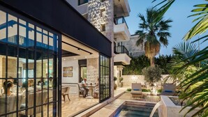 A modern outdoor pool area with a stone wall, seating, and a view of the dining area. - Boutique Hotel Casa del Mare - Mediterraneo (Kamenari)