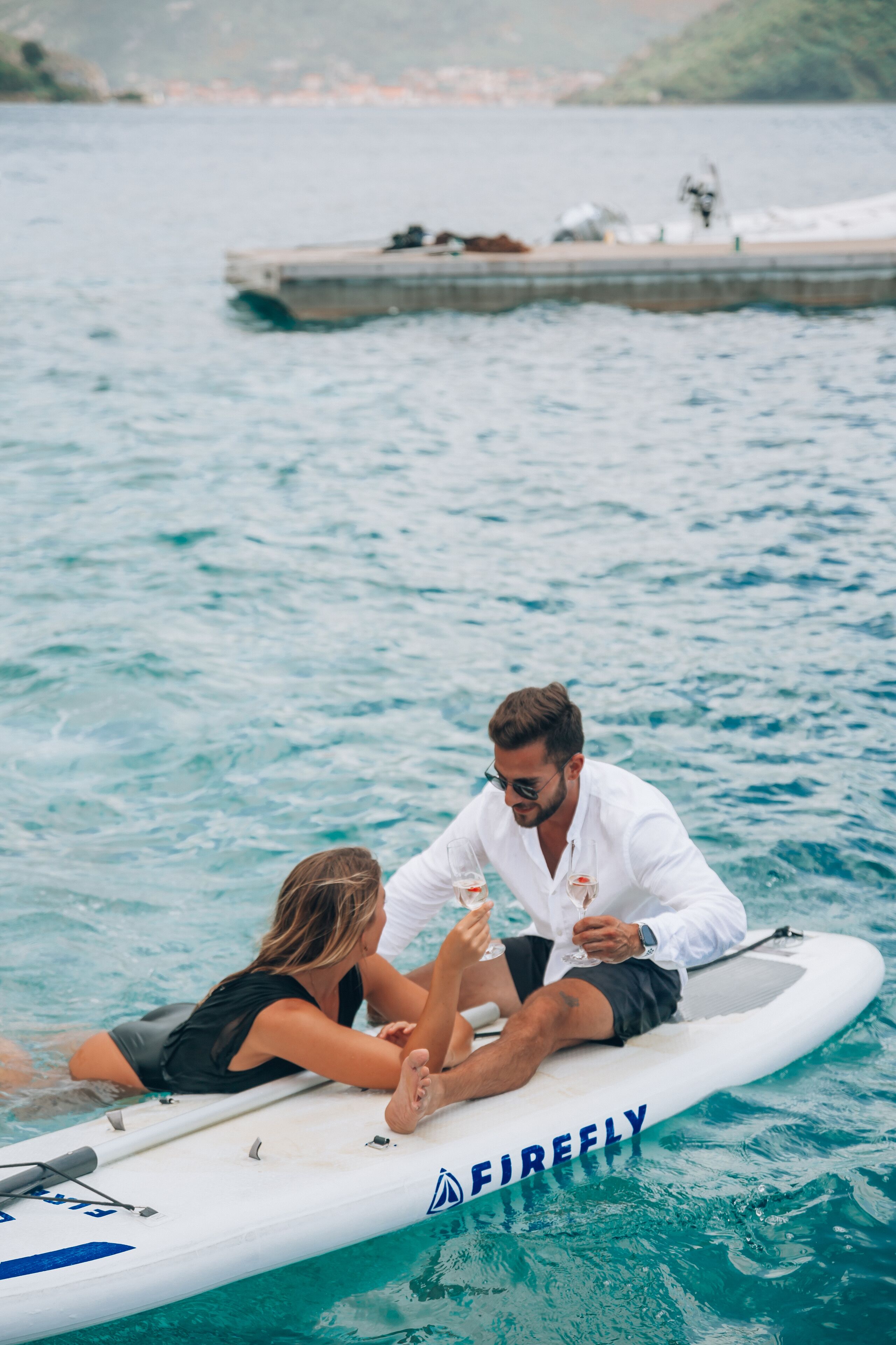 A couple on a white inflatable boat with "FIREFLY" written on it, floating on calm water.