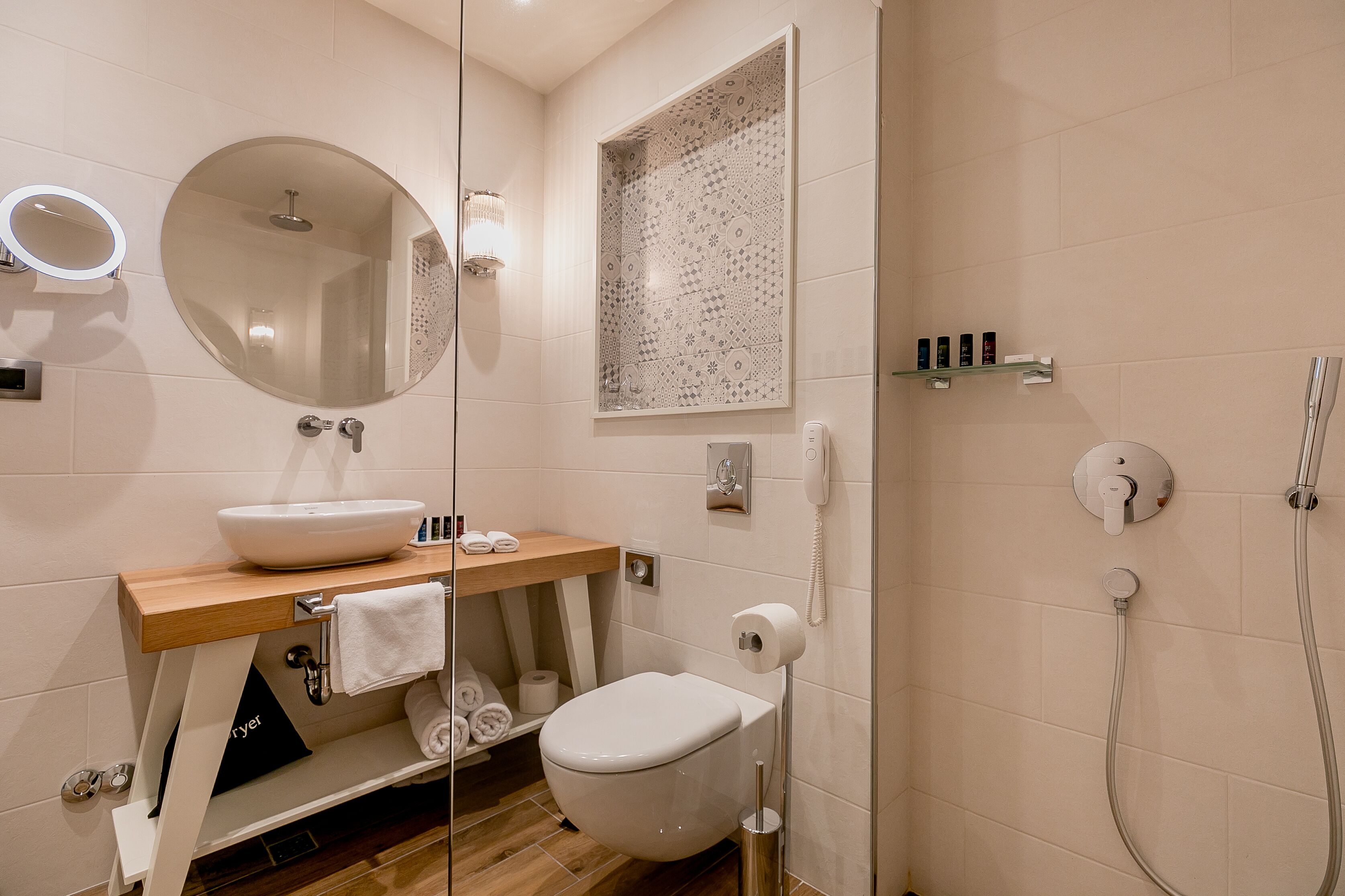 Un bagno moderno con uno specchio rotondo, un lavandino, un water e una doccia.