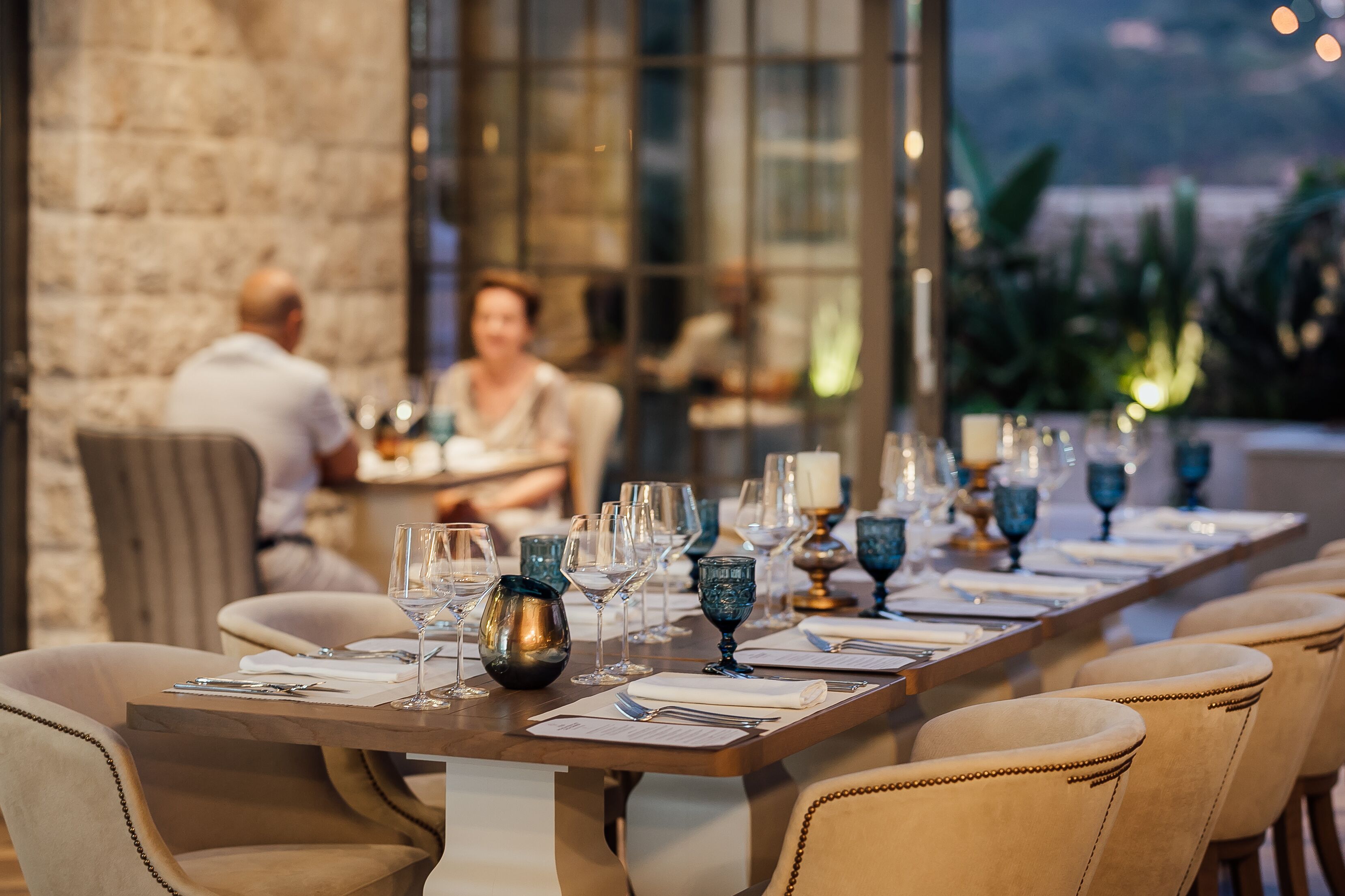 Mesa lista para una comida, con sillas, un muro de piedra y vistas al exterior.
