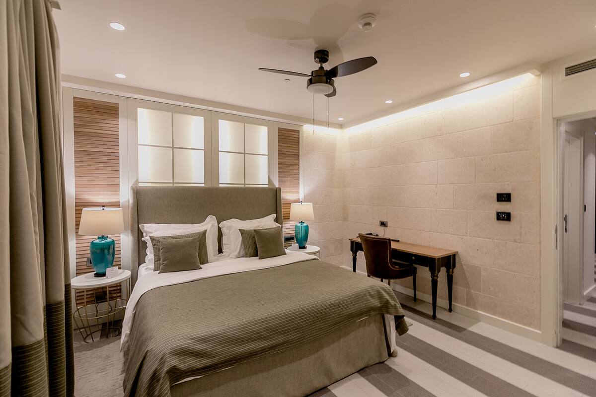 A modern hotel room with a large bed, a desk, and a ceiling fan.