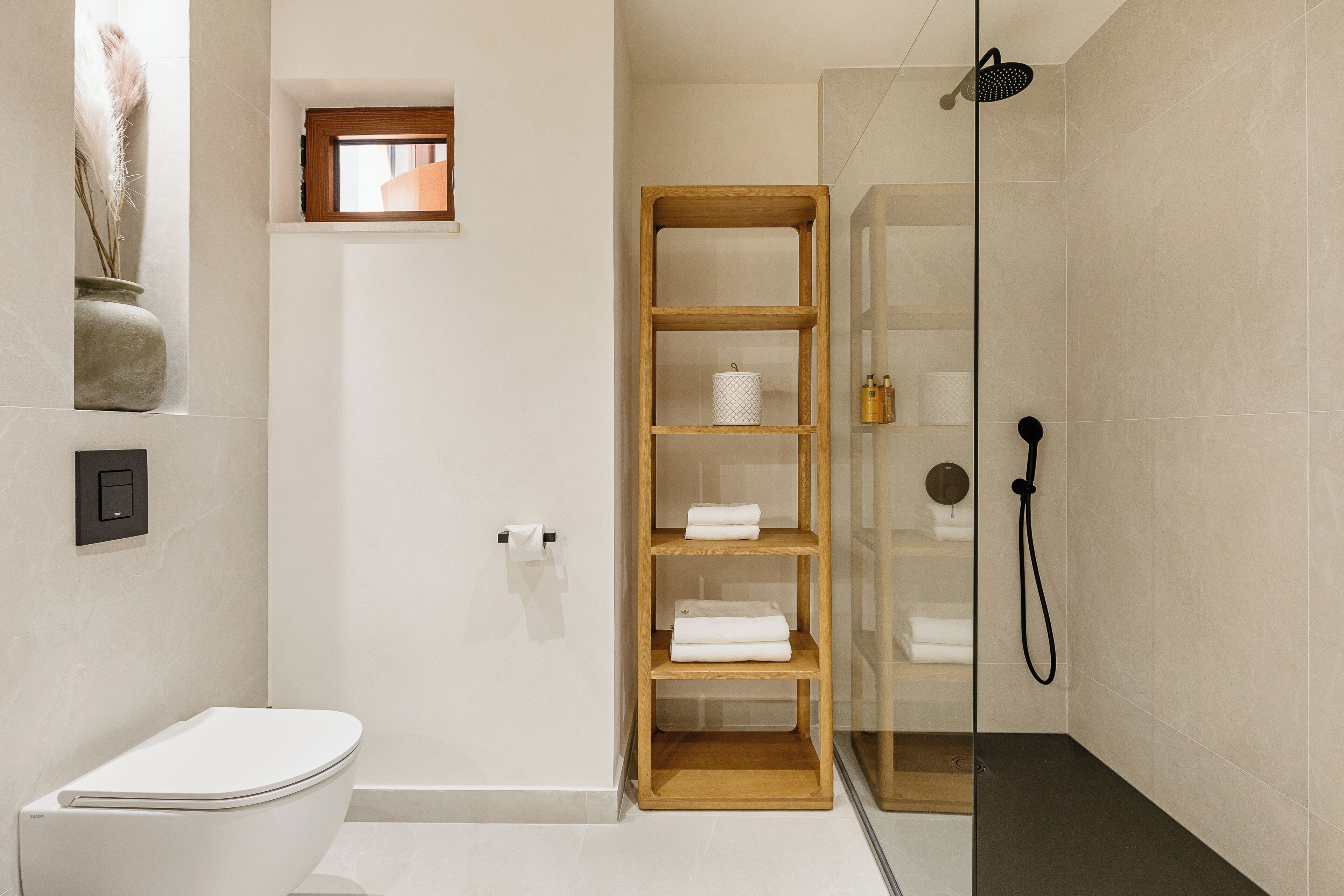 Un baño moderno con inodoro, ducha de vidrio y repisa de madera con toallas.