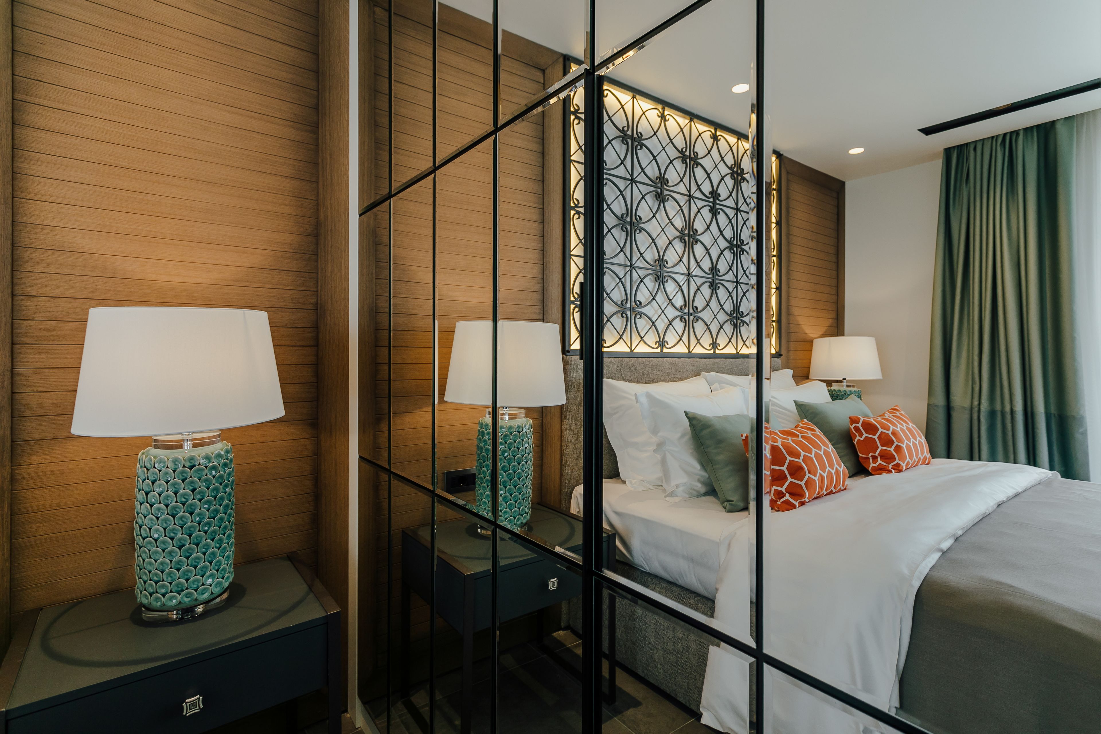 Une chambre d’hôtel moderne avec un mur lambrissé en bois, une tête de lit décorative en métal, un lit avec une literie blanche et des oreillers colorés, ainsi que deux lampes de chevet.