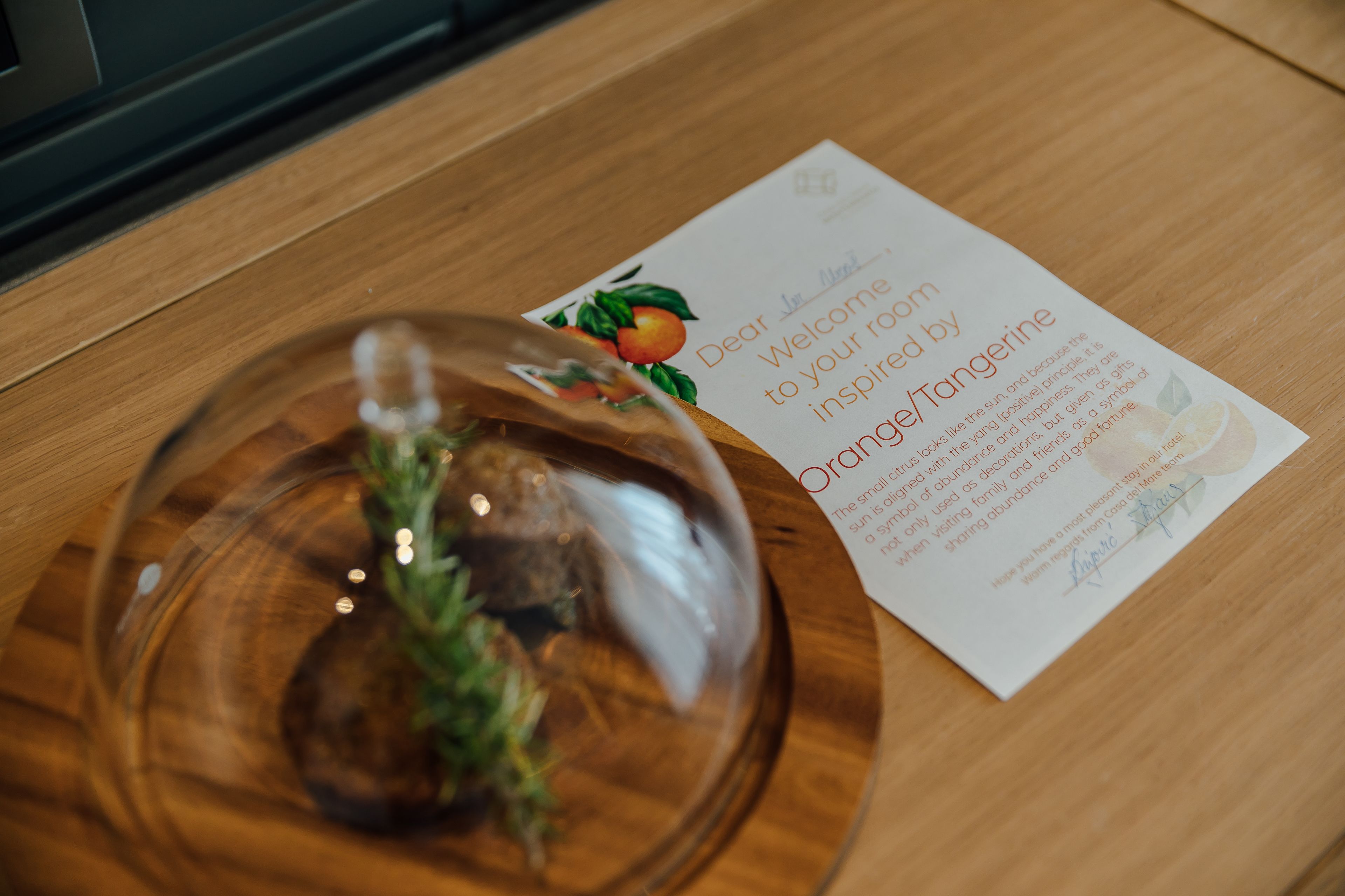 Una mesa de madera con una cúpula de vidrio sobre una planta y una tarjeta de bienvenida.