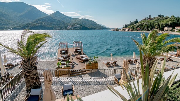 A seaside terrace with wooden deck seating, palm trees, and a view of the sea and mountains. - Boutique Hotel Casa del Mare - Mediterraneo (Kamenari)