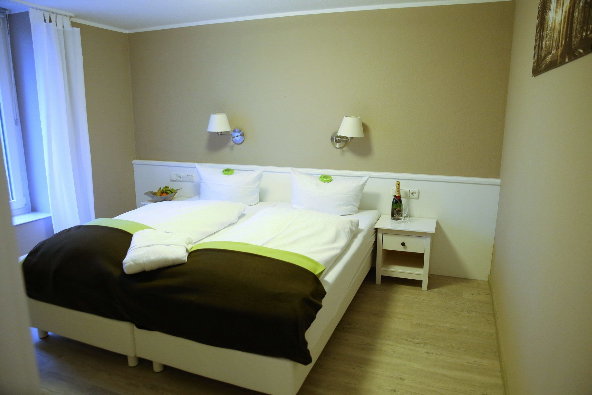 Une chambre d’hôtel avec un lit, des tables de chevet, une commode et une fenêtre avec des rideaux.