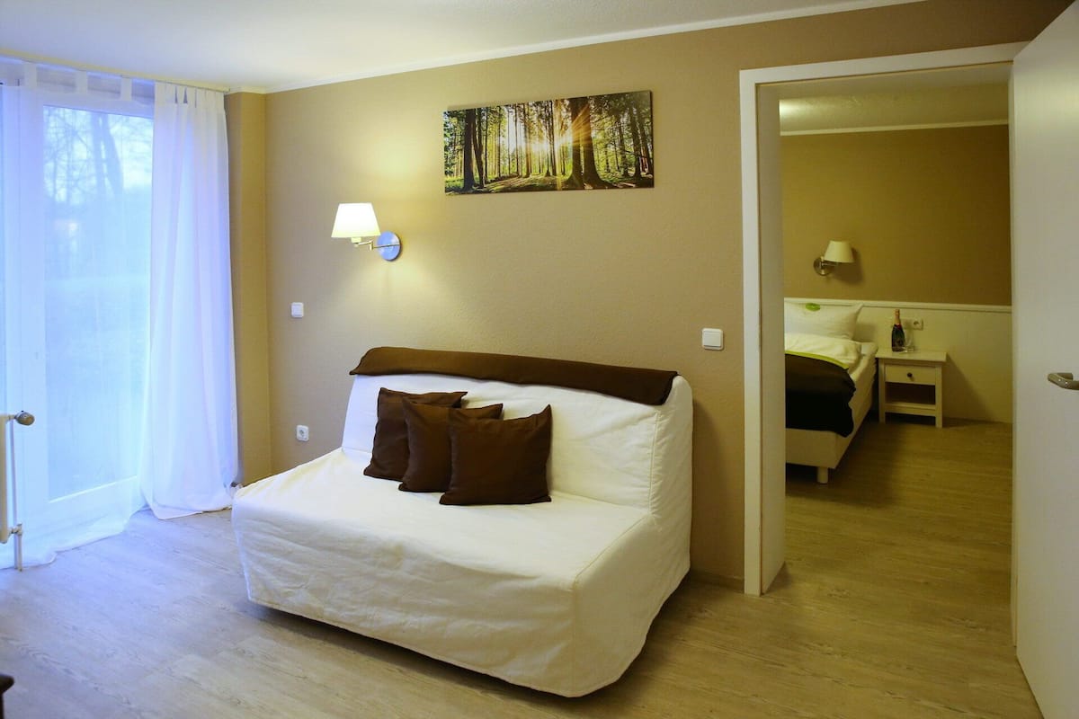 A hotel room with a bed, a painting of a forest, and a door leading to another room.