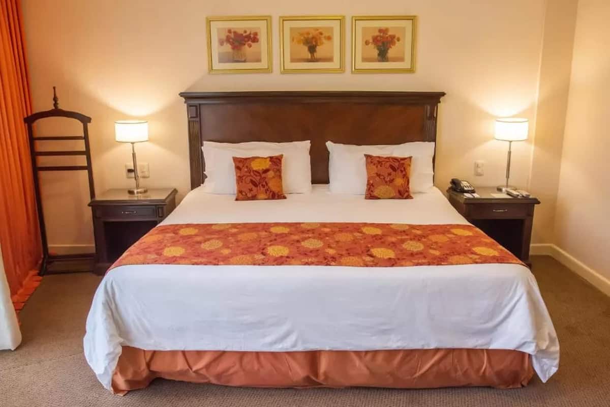 A hotel room with a large bed, two bedside tables, a wooden headboard, and three framed pictures on the wall.