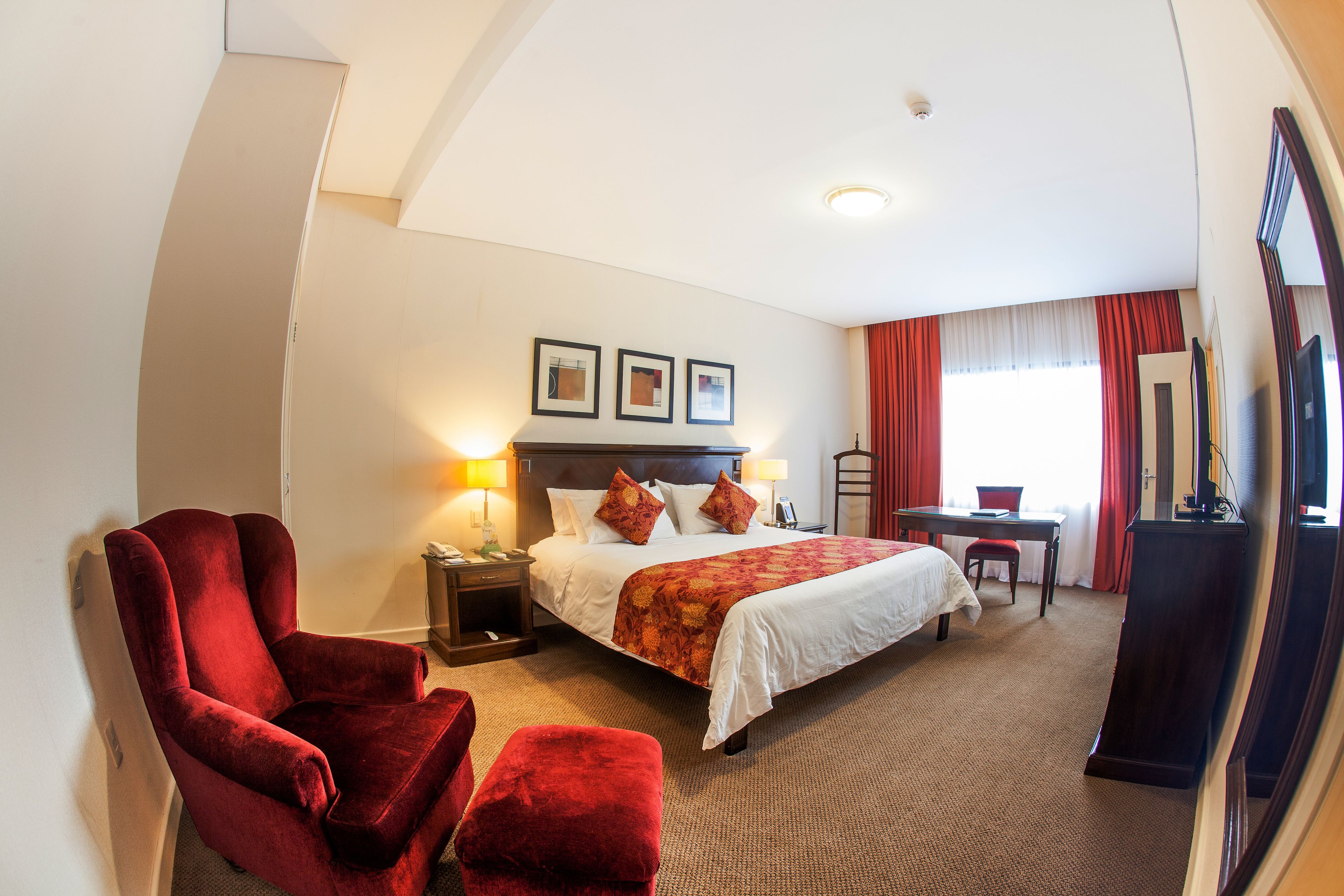 Une chambre d’hôtel avec un grand lit, un fauteuil rouge, un bureau et un miroir.