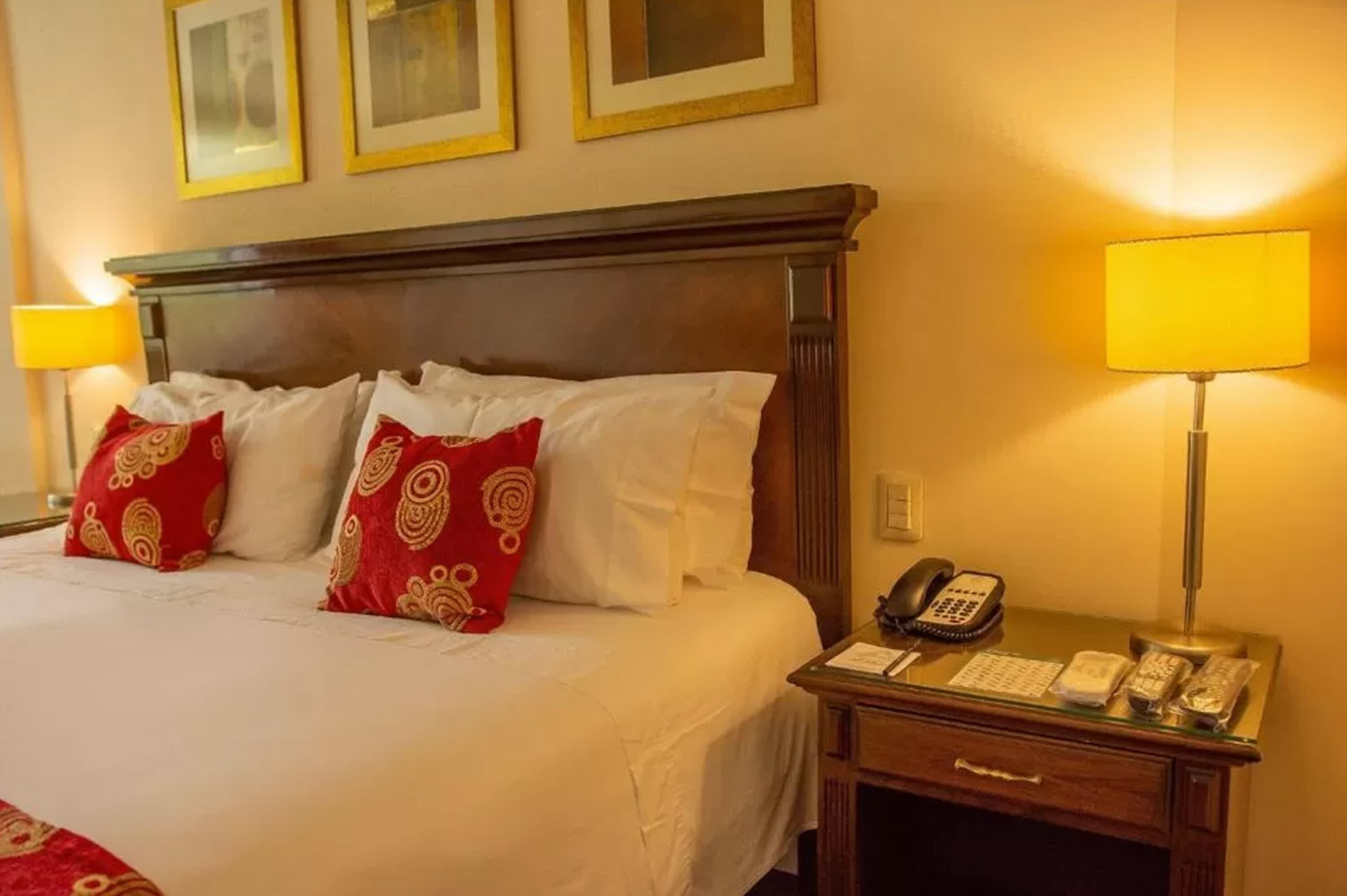 A hotel room with a large bed, two bedside lamps, a telephone, and a small desk with a lamp.