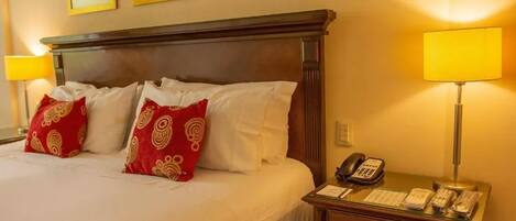 Quarto de hotel com uma cama grande, duas luminárias de cabeceira, um telefone e uma pequena escrivaninha com abajur.