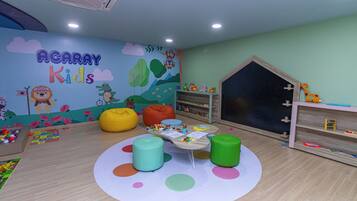 Un cuarto de juegos infantil con un mural, pufs, una mesita y estanterías llenas de juguetes.