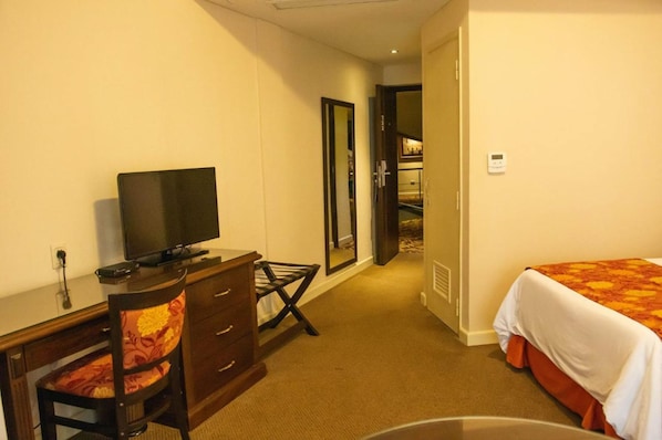 A hotel room with a bed, a desk with a television, a chair, and a mirror. - Hotel Casino Acaray (Ciudad Del Este)