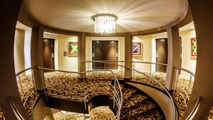 A hotel lobby with a central staircase, a chandelier, and artwork on the walls. - Hotel Casino Acaray (Ciudad Del Este)