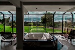 A modern bathroom with a large bathtub, two chairs, and a view of a landscaped garden through large windows. - Hotel Casino Acaray (Ciudad Del Este)
