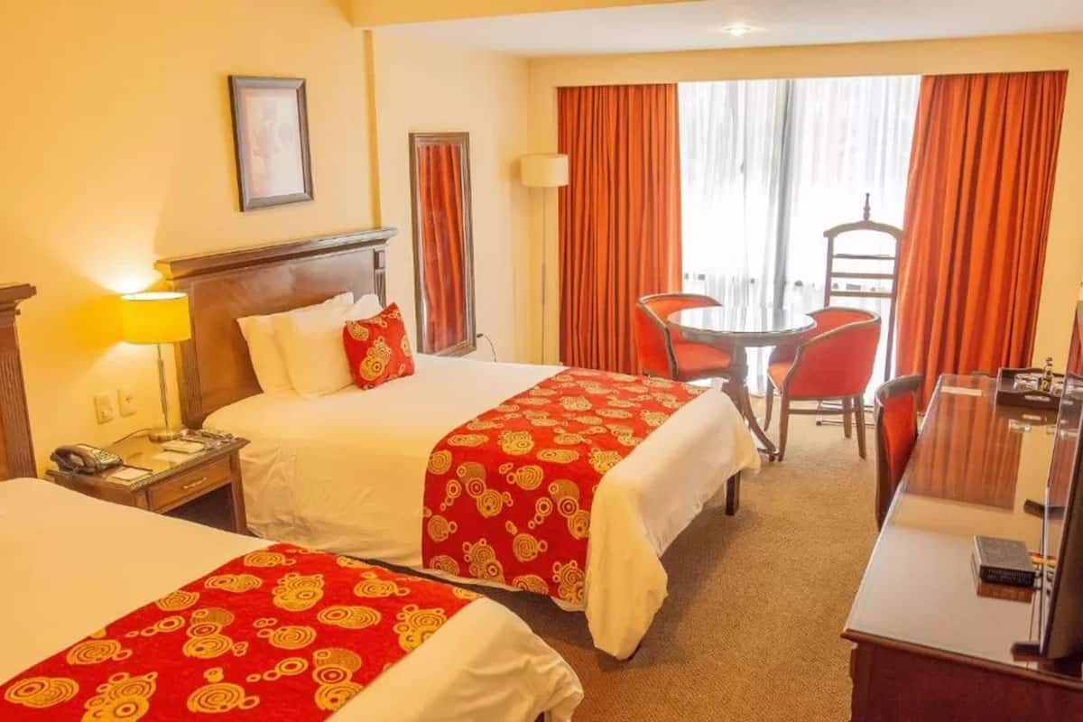 A hotel room with two beds, a desk, a chair, and a window with curtains.