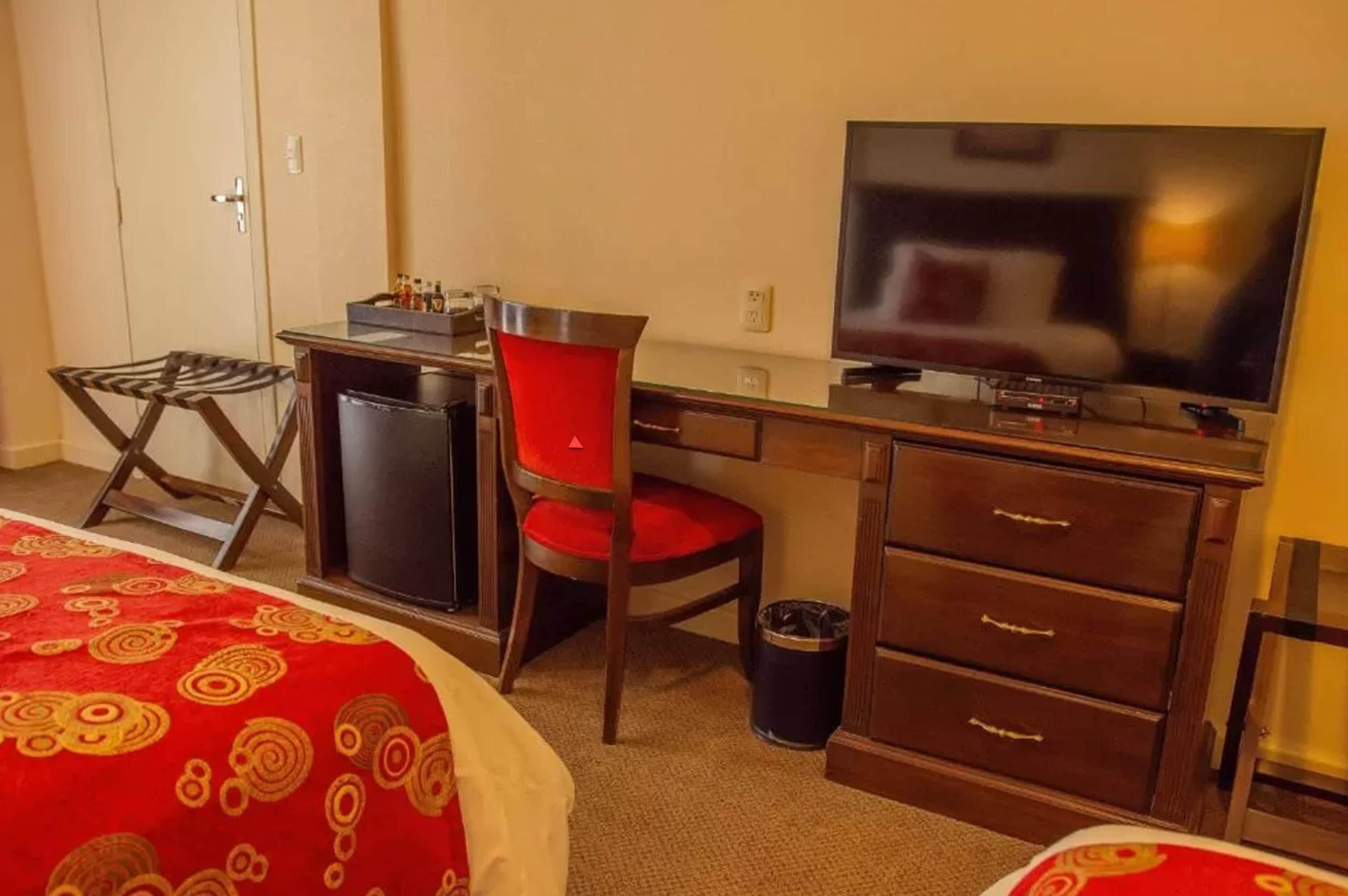 A hotel room with a bed, a desk with a chair, a television, and a minibar.
